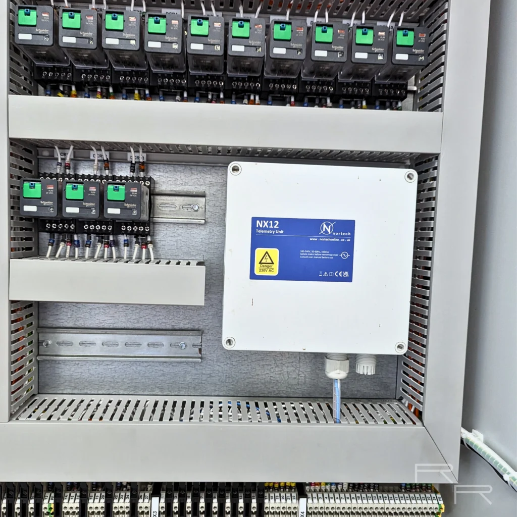 Nortech NX12 telemetry unit mounted beside three 24VDC output relays, with numbered field terminal rails running below