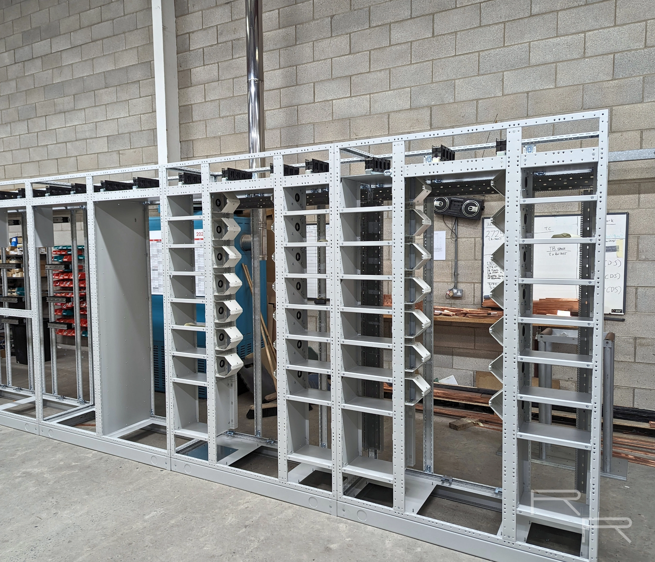 Empty motor control centre cubicle frames on the build floor with busbar supports and gear trays fitted